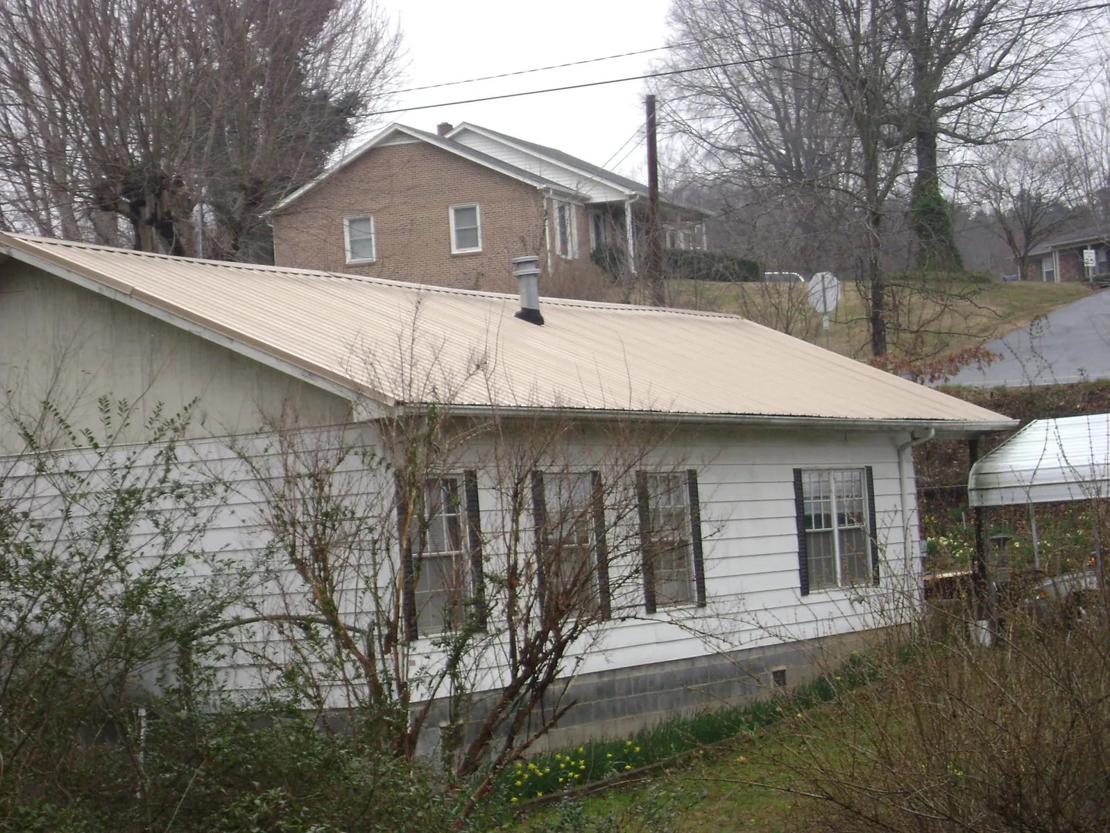 Tan metal roof on a white sided house set into a hillside — Commercial Roofing by Roofing Brothers in Hinsdale